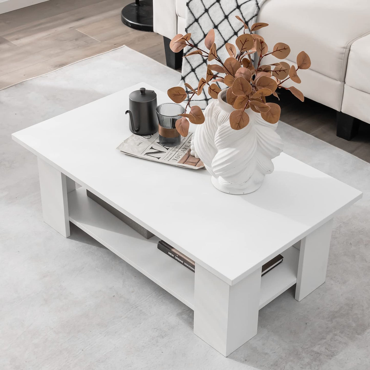 White coffee table with a vase of leaves, coffee mug, and newspaper in a living room setting.