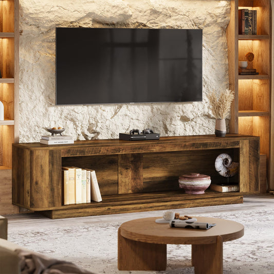 A rustic dark brown wooden TV stand console with open shelving, styled in a living room setting with a stone wall, a mounted flat-screen TV, a round wooden coffee table, and warm ambient lighting.