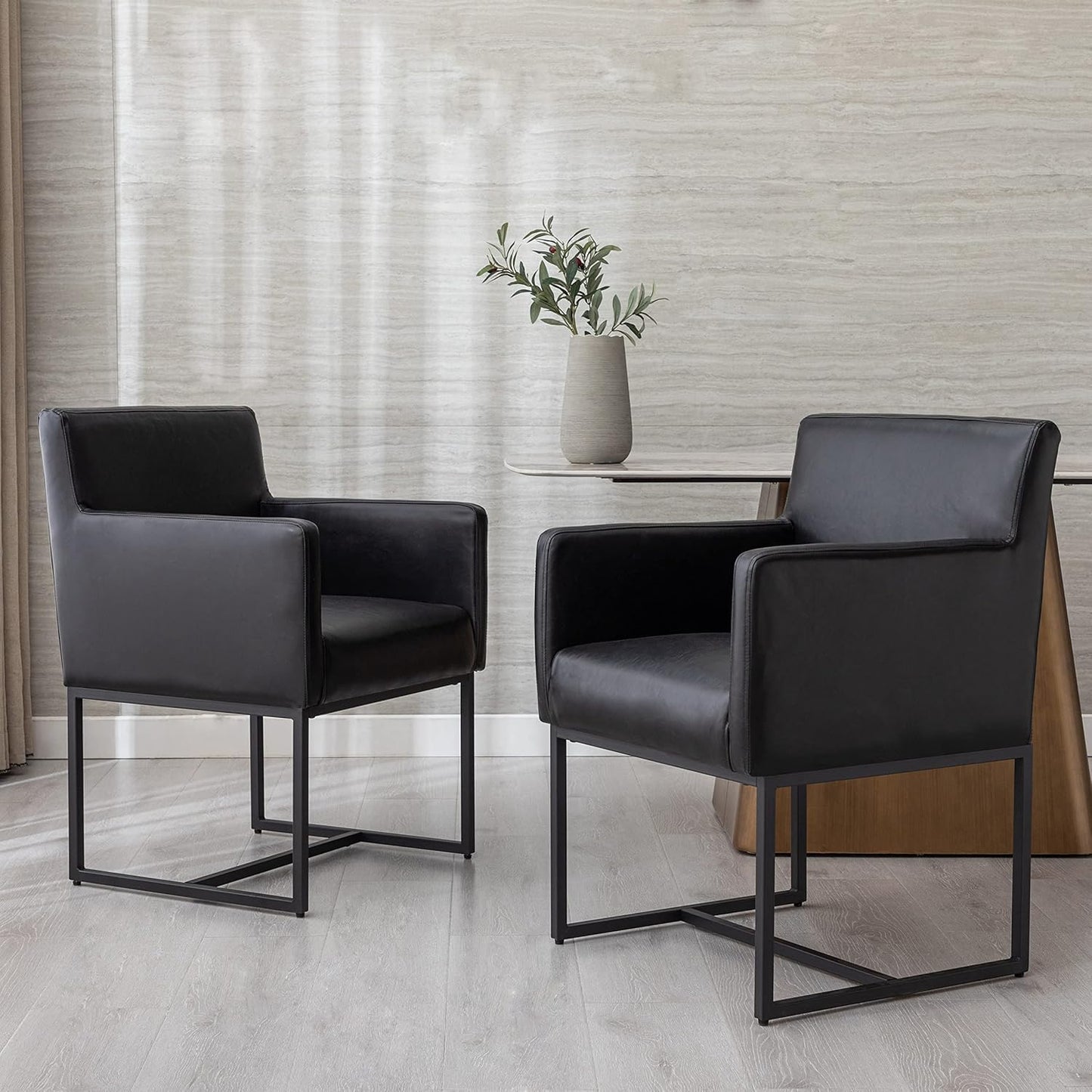 Two black chairs in a modern interior setting with a vase and plant on a table.