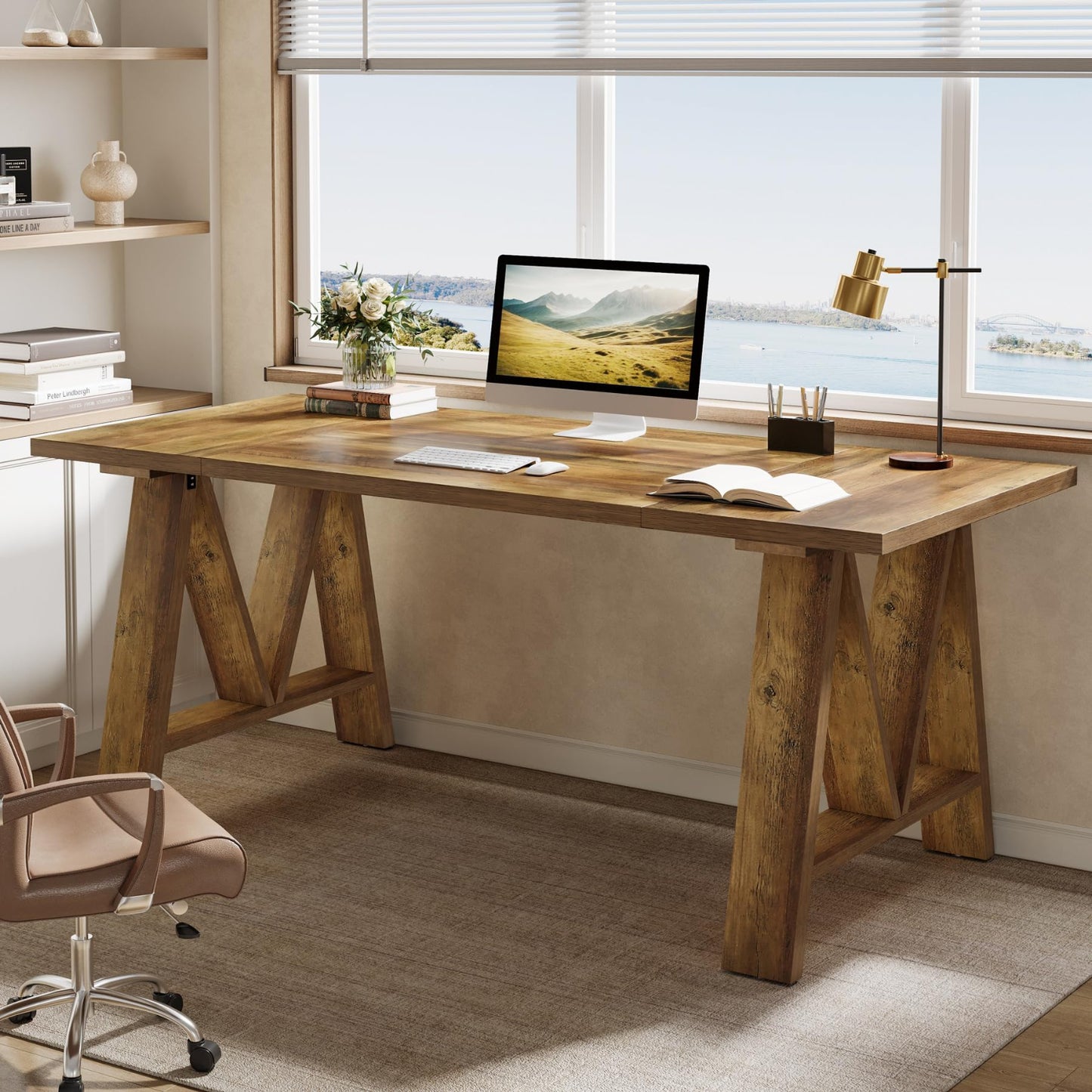 Wooden desk with office items in a bright room with large windows.