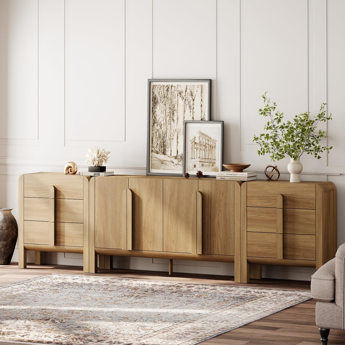 A light oak wood sideboard credenza styled in a modern living room setting with a patterned area rug, decorative framed art, and a potted plant against a white paneled wall.