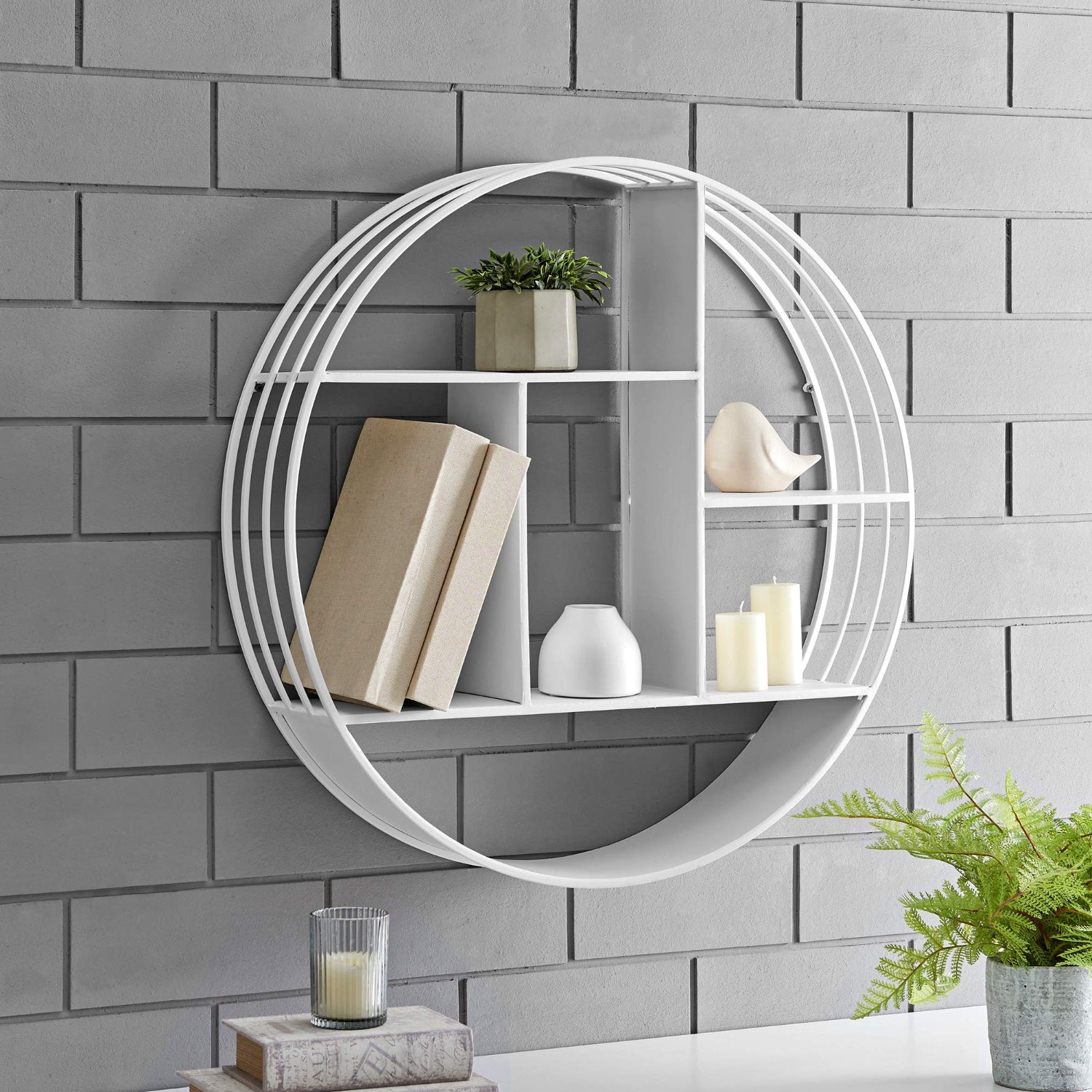 Round white wall shelf with decorative items against a gray brick wall.